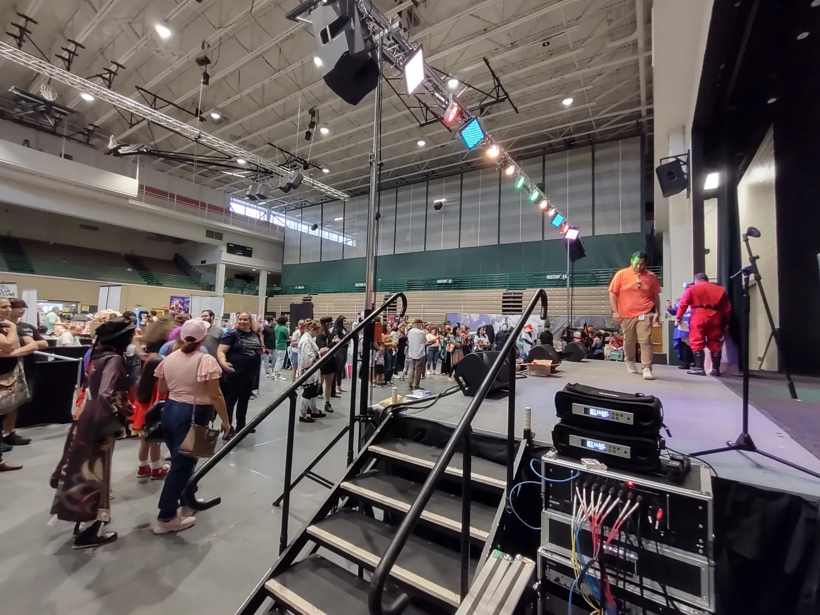 Indoor event with stage lighting on overhead truss, amplifier racks and cabling beside the stage steps