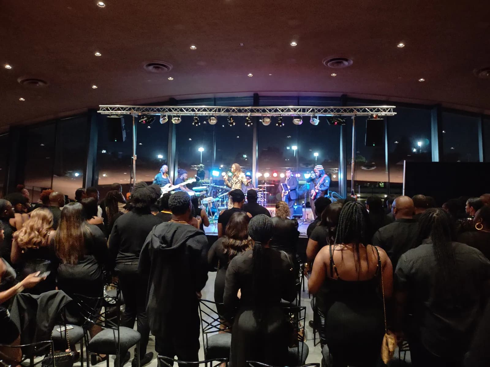 Band performing on a lit indoor stage in front of an audience of guests standing in an evening venue